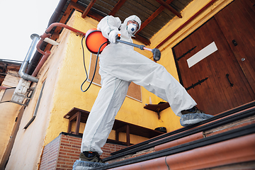 Image showing Coronavirus Pandemic. A disinfector in a protective suit and mask sprays disinfectants in the house or office