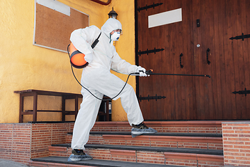 Image showing Coronavirus Pandemic. A disinfector in a protective suit and mask sprays disinfectants in the house or office