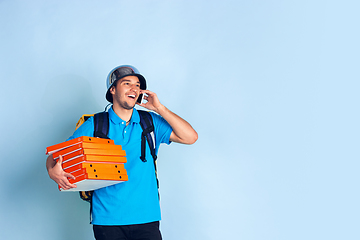 Image showing Contacless delivery service during quarantine. Man delivers food and shopping bags during insulation. Emotions of deliveryman isolated on blue background.