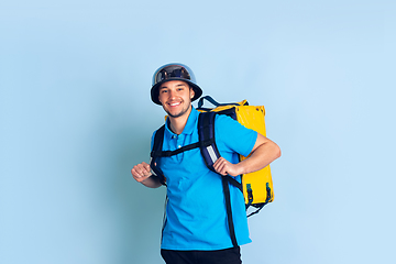 Image showing Contacless delivery service during quarantine. Man delivers food and shopping bags during insulation. Emotions of deliveryman isolated on blue background.