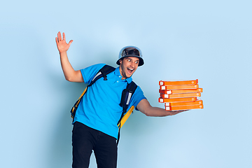 Image showing Contacless delivery service during quarantine. Man delivers food and shopping bags during insulation. Emotions of deliveryman isolated on blue background.