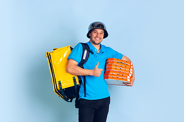 Image showing Contacless delivery service during quarantine. Man delivers food and shopping bags during insulation. Emotions of deliveryman isolated on blue background.