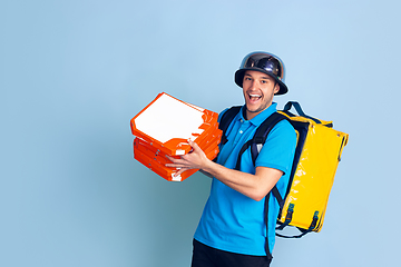 Image showing Contacless delivery service during quarantine. Man delivers food and shopping bags during insulation. Emotions of deliveryman isolated on blue background.