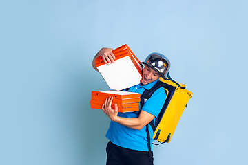 Image showing Contacless delivery service during quarantine. Man delivers food and shopping bags during insulation. Emotions of deliveryman isolated on blue background.