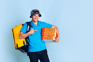 Image showing Contacless delivery service during quarantine. Man delivers food and shopping bags during insulation. Emotions of deliveryman isolated on blue background.