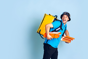 Image showing Contacless delivery service during quarantine. Man delivers food and shopping bags during insulation. Emotions of deliveryman isolated on blue background.