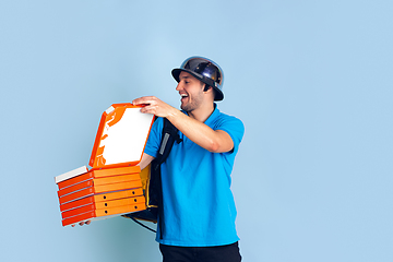 Image showing Contacless delivery service during quarantine. Man delivers food and shopping bags during insulation. Emotions of deliveryman isolated on blue background.