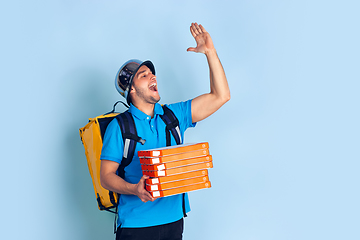 Image showing Contacless delivery service during quarantine. Man delivers food and shopping bags during insulation. Emotions of deliveryman isolated on blue background.