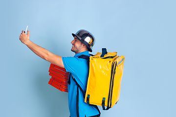 Image showing Contacless delivery service during quarantine. Man delivers food and shopping bags during insulation. Emotions of deliveryman isolated on blue background.