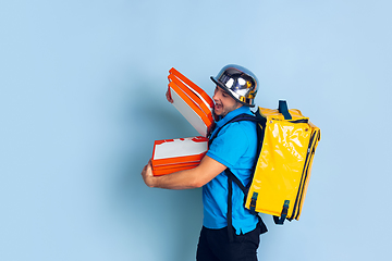 Image showing Contacless delivery service during quarantine. Man delivers food and shopping bags during insulation. Emotions of deliveryman isolated on blue background.