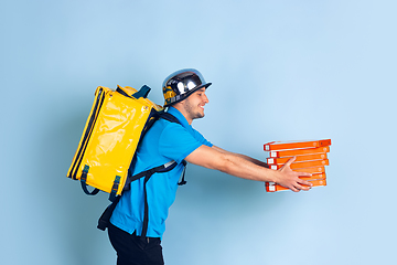 Image showing Contacless delivery service during quarantine. Man delivers food and shopping bags during insulation. Emotions of deliveryman isolated on blue background.