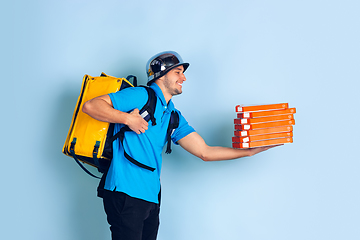 Image showing Contacless delivery service during quarantine. Man delivers food and shopping bags during insulation. Emotions of deliveryman isolated on blue background.