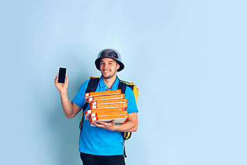 Image showing Contacless delivery service during quarantine. Man delivers food and shopping bags during insulation. Emotions of deliveryman isolated on blue background.