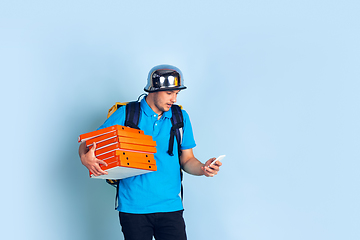 Image showing Contacless delivery service during quarantine. Man delivers food and shopping bags during insulation. Emotions of deliveryman isolated on blue background.