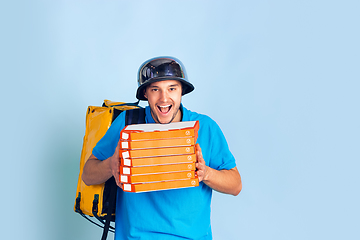 Image showing Contacless delivery service during quarantine. Man delivers food and shopping bags during insulation. Emotions of deliveryman isolated on blue background.