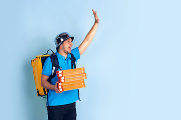 Image showing Contacless delivery service during quarantine. Man delivers food and shopping bags during insulation. Emotions of deliveryman isolated on blue background.