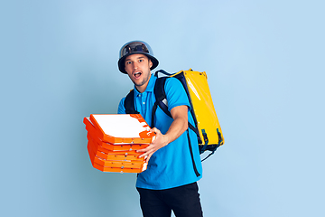 Image showing Contacless delivery service during quarantine. Man delivers food and shopping bags during insulation. Emotions of deliveryman isolated on blue background.