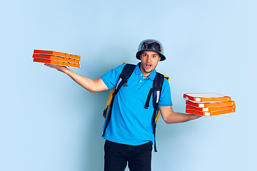 Image showing Contacless delivery service during quarantine. Man delivers food and shopping bags during insulation. Emotions of deliveryman isolated on blue background.