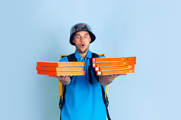 Image showing Contacless delivery service during quarantine. Man delivers food and shopping bags during insulation. Emotions of deliveryman isolated on blue background.