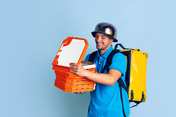 Image showing Contacless delivery service during quarantine. Man delivers food and shopping bags during insulation. Emotions of deliveryman isolated on blue background.