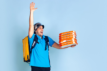 Image showing Contacless delivery service during quarantine. Man delivers food and shopping bags during insulation. Emotions of deliveryman isolated on blue background.