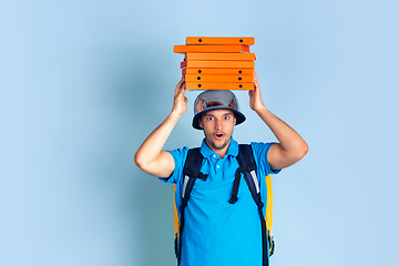 Image showing Contacless delivery service during quarantine. Man delivers food and shopping bags during insulation. Emotions of deliveryman isolated on blue background.