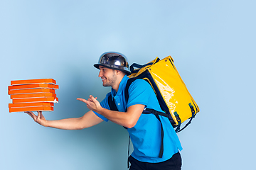 Image showing Contacless delivery service during quarantine. Man delivers food and shopping bags during insulation. Emotions of deliveryman isolated on blue background.