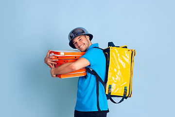 Image showing Contacless delivery service during quarantine. Man delivers food and shopping bags during insulation. Emotions of deliveryman isolated on blue background.