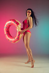 Image showing Fashion portrait of young fit and sportive woman in stylish pink luxury swimwear with rubber donut on gradient background. Perfect body ready for summertime.