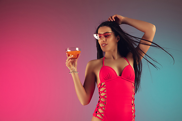 Image showing Fashion portrait of young fit and sportive woman in stylish pink luxury swimwear with cocktail on gradient background. Perfect body ready for summertime.