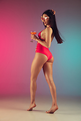 Image showing Fashion portrait of young fit and sportive woman in stylish pink luxury swimwear with cocktail on gradient background. Perfect body ready for summertime.