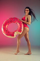Image showing Fashion portrait of young fit and sportive woman in stylish pink luxury swimwear with rubber donut on gradient background. Perfect body ready for summertime.