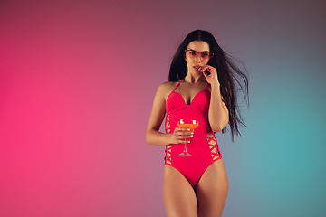 Image showing Fashion portrait of young fit and sportive woman in stylish pink luxury swimwear with cocktail on gradient background. Perfect body ready for summertime.