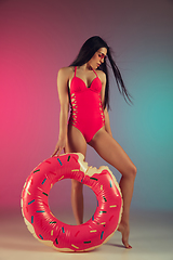 Image showing Fashion portrait of young fit and sportive woman in stylish pink luxury swimwear with rubber donut on gradient background. Perfect body ready for summertime.