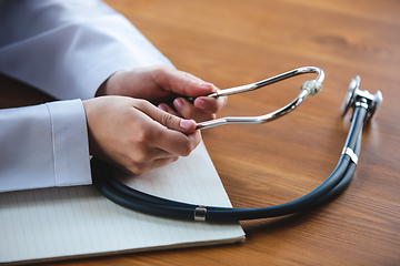 Image showing Close up of doctors hands with stethoscope, sheets and pills on wooden background