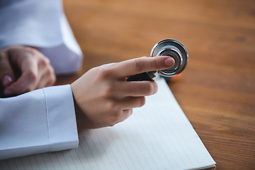 Image showing Close up of doctors hands with stethoscope, sheets and pills on wooden background