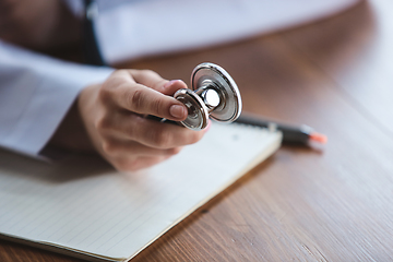 Image showing Close up of doctors hands with stethoscope, sheets and pills on wooden background