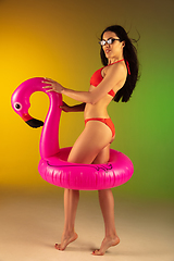 Image showing Fashion portrait of young fit and sportive woman in stylish red luxury swimwear with rubber flamingo on gradient background. Perfect body ready for summertime.