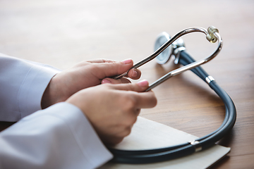 Image showing Close up of doctors hands with stethoscope, sheets and pills on wooden background