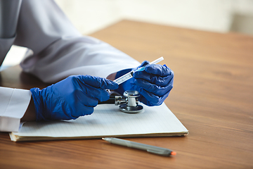 Image showing Close up of doctors hands wearing blue protective gloves with stethoscope and syringe on wooden table background