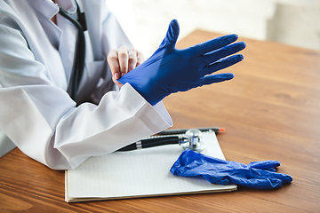 Image showing Close up of doctors hands wearing blue protective gloves on wooden table background