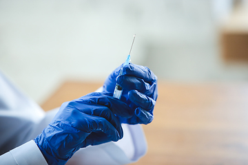 Image showing Close up of doctors hands wearing blue protective gloves with syringe on wooden table background