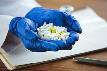 Image showing Close up of doctors hands wearing blue protective gloves giving bunch of pills on wooden table background