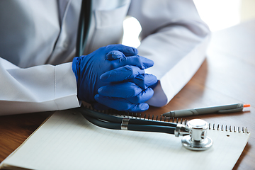 Image showing Close up of doctors hands wearing blue protective gloves with stethoscope on wooden table background