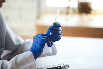 Image showing Close up of doctors hands wearing blue protective gloves with stethoscope and syringe on wooden table background