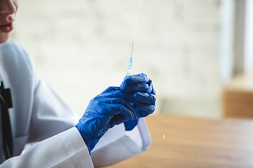 Image showing Close up of doctors hands wearing blue protective gloves with syringe on wooden table background