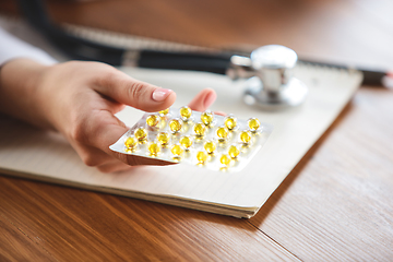 Image showing Close up of doctors hands with stethoscope, sheets, giving pills to patient on wooden background