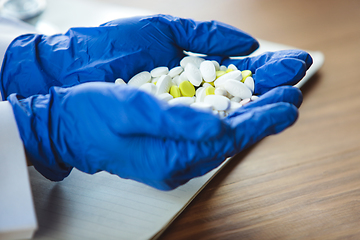 Image showing Close up of doctors hands wearing blue protective gloves giving bunch of pills on wooden table background