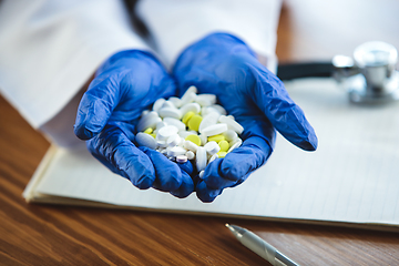 Image showing Close up of doctors hands wearing blue protective gloves giving bunch of pills on wooden table background