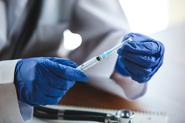 Image showing Close up of doctors hands wearing blue protective gloves with stethoscope and syringe on wooden table background